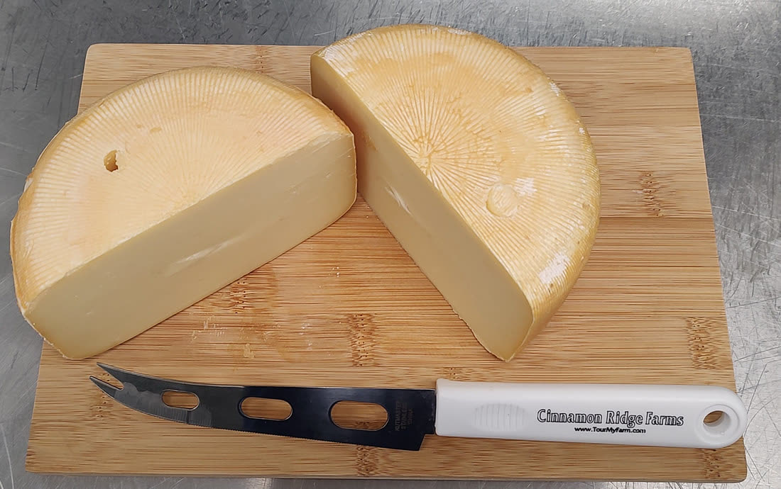 A cut wheel of farmstead cheese with a Cinnamon Ridge Farms knife