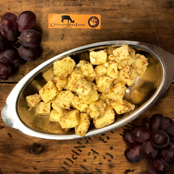 Seasoned cheese curds in a silver dish beside grapes